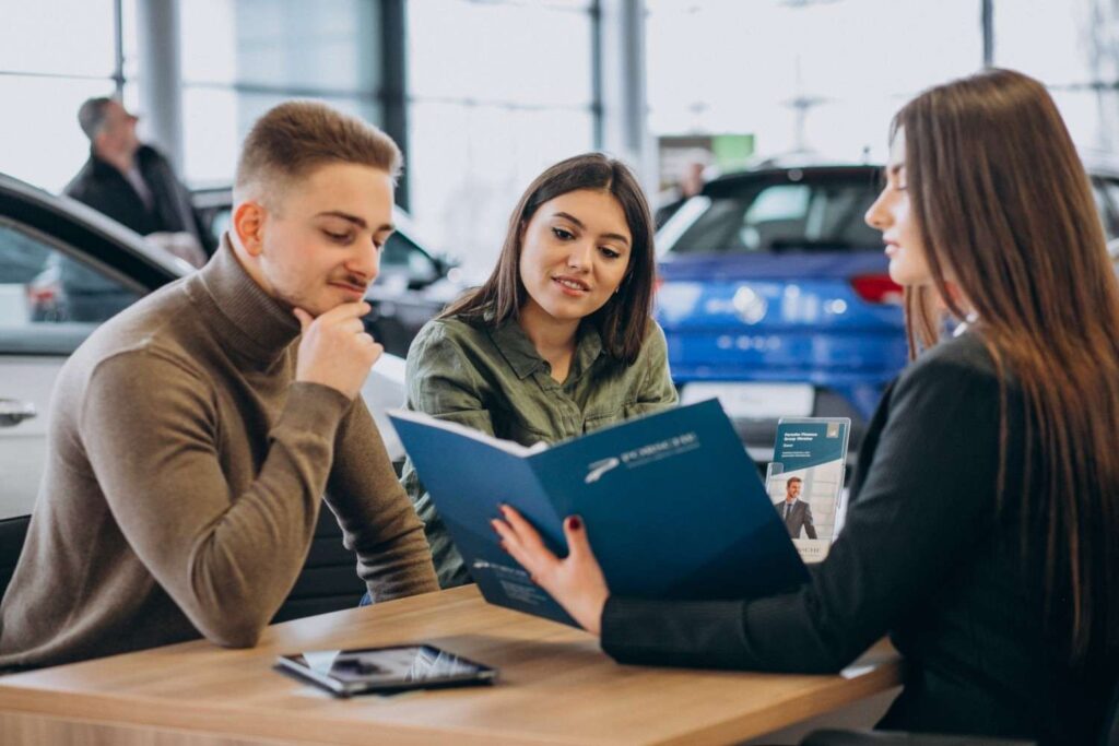 Young couple talking to a car salesperson in showroom, illustrating One Big Beautiful Bill Act (OBBBA) IRS auto loan interest deduction