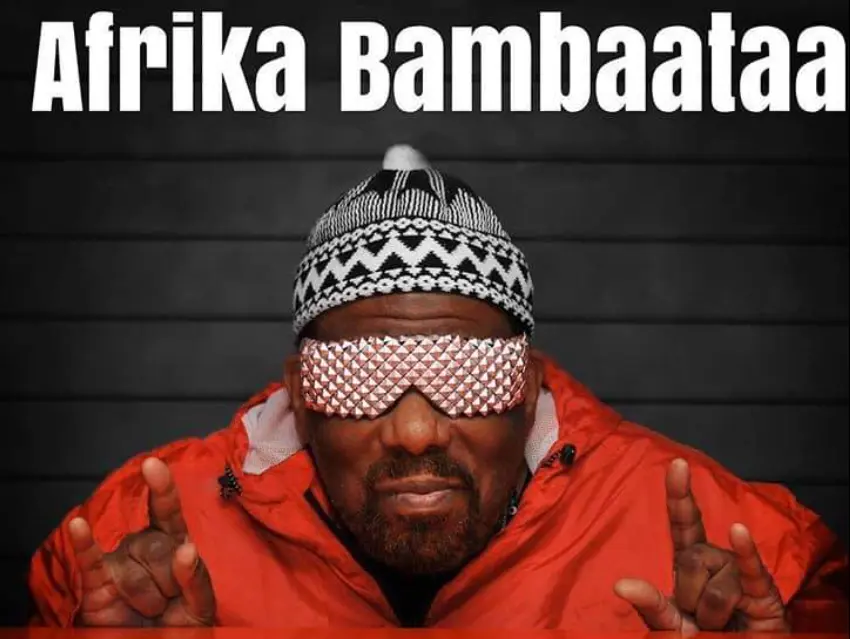 Afrika Bambaataa wearing a red jacket and patterned sunglasses with his name displayed above