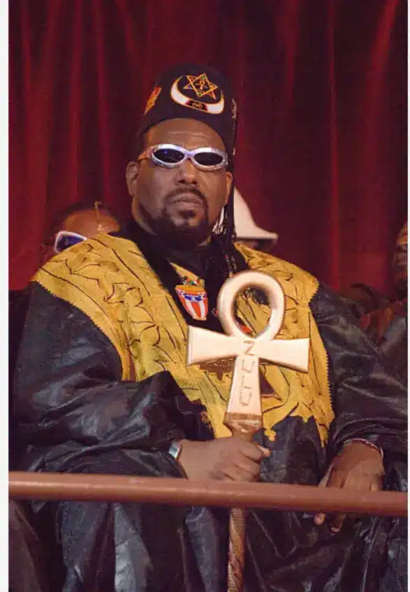 Afrika Bambaataa seated wearing ceremonial clothing and holding an ankh symbol representing the Universal Zulu Nation