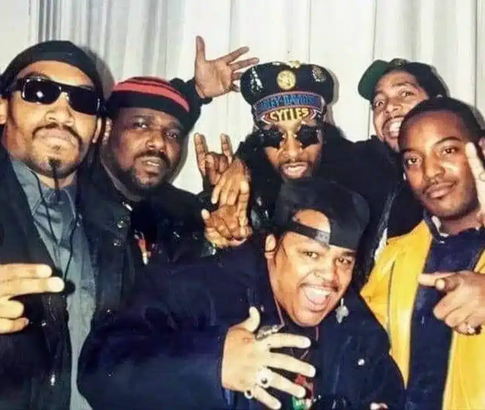 Afrika Bambaataa posing with members of a hip-hop group wearing hats and sunglasses in a casual setting